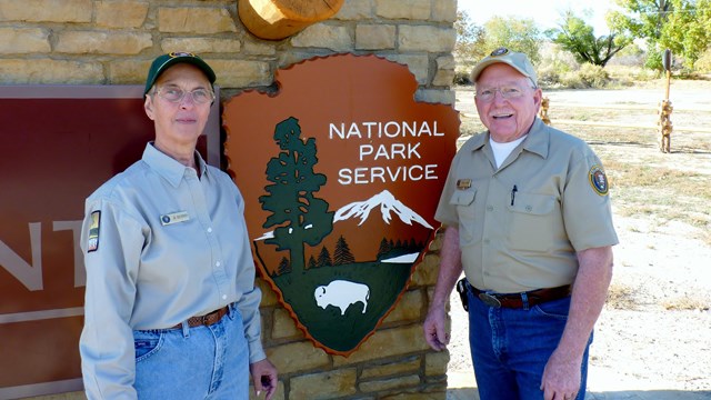 Two park volunteers wearing tan VIP uniforms standing on either side of an arrowhead.