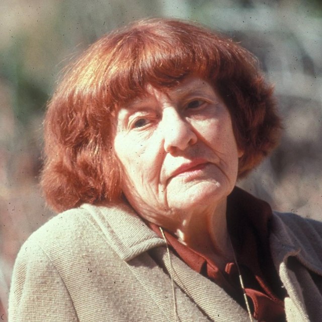 A color photo of a woman with red hair sitting outdoors.
