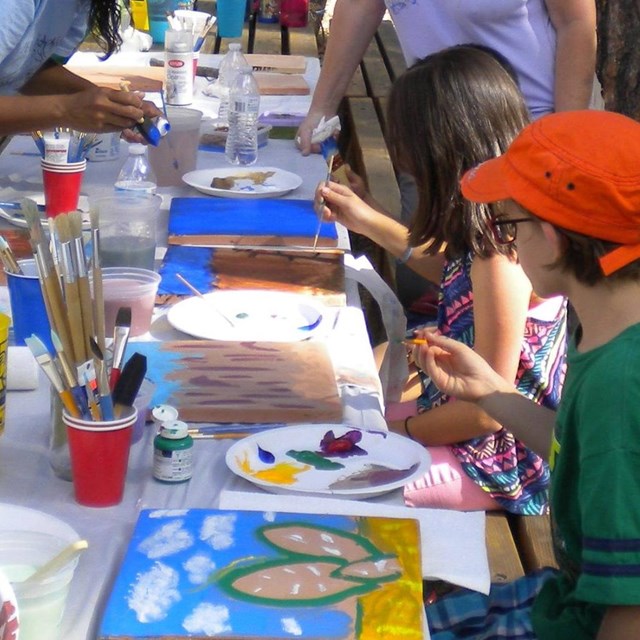 A group of children and adults painting outdoors. 