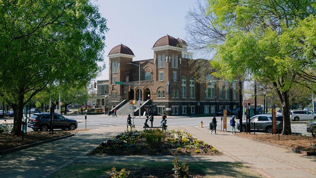 A large brick church with domes with a statue of 4 girls in a park.