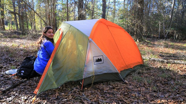 a woman sitting next to a tent in the forest