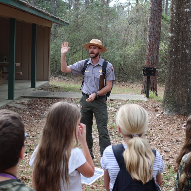 a ranger holding up a hand while talking to students in a picnic area.