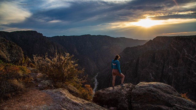 A person standing on a canyon edge looking at a sunset