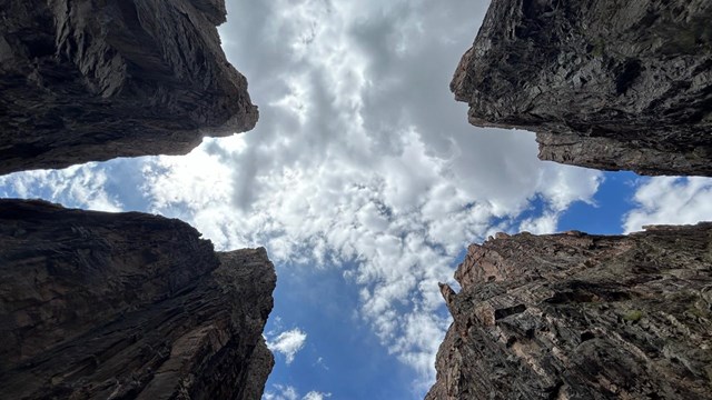 Image of a view looking up. Four canyon wall segments are straight above towards a blue sky