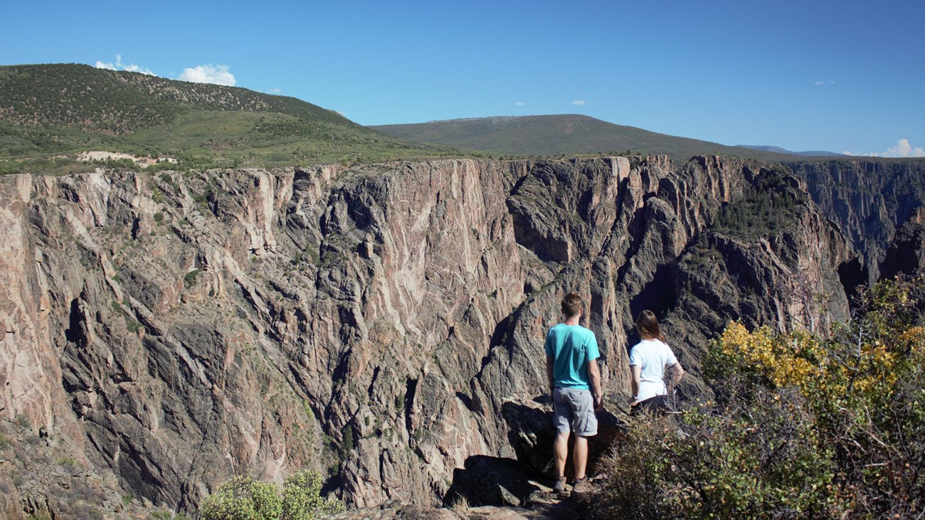 Two people standing at an overlook facing a dark, steep canyon