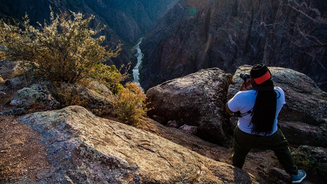 A person holding a camera while taking a picture of a canyon and rocky cliffs