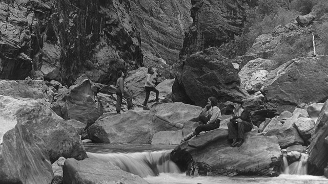 A group of people sitting on large boulders next to a river in a canyon