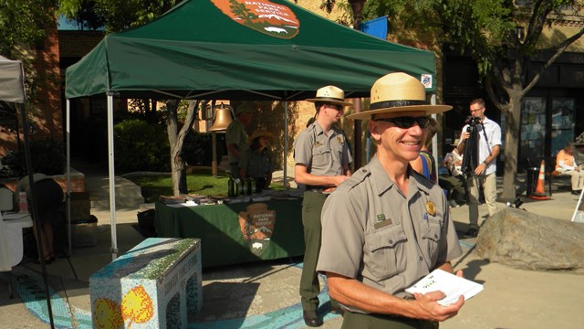 Two park rangers in uniform at an information booth with a green covering