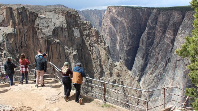 People standing at a fenced overlook by a large canyon