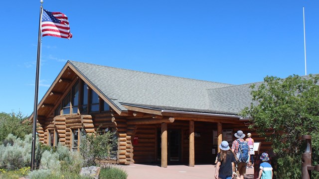 A wooden cabin style visitor center with people walking towards it and a flag flying above