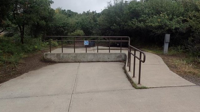 A concrete ramp, handrail, and camping area with a blue accessibility sign