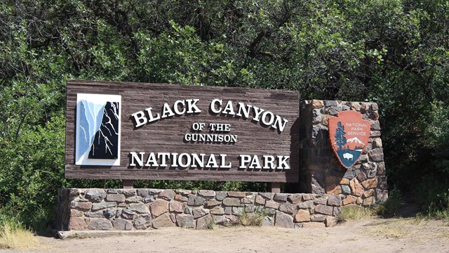 A large park entrance sign with white lettering and a graphic of a canyon