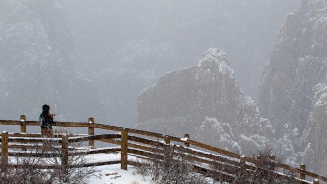 A person stands at an overlook with wooden fencing covered in snow