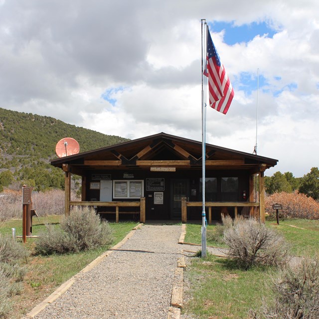 A wooden ranger station building with a porch. A flag, pole, and path are in front of the building