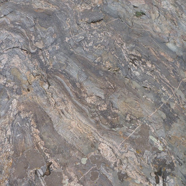 Image of metamorphic rock with grey, brown, blue, and lighter colored sections swirled together