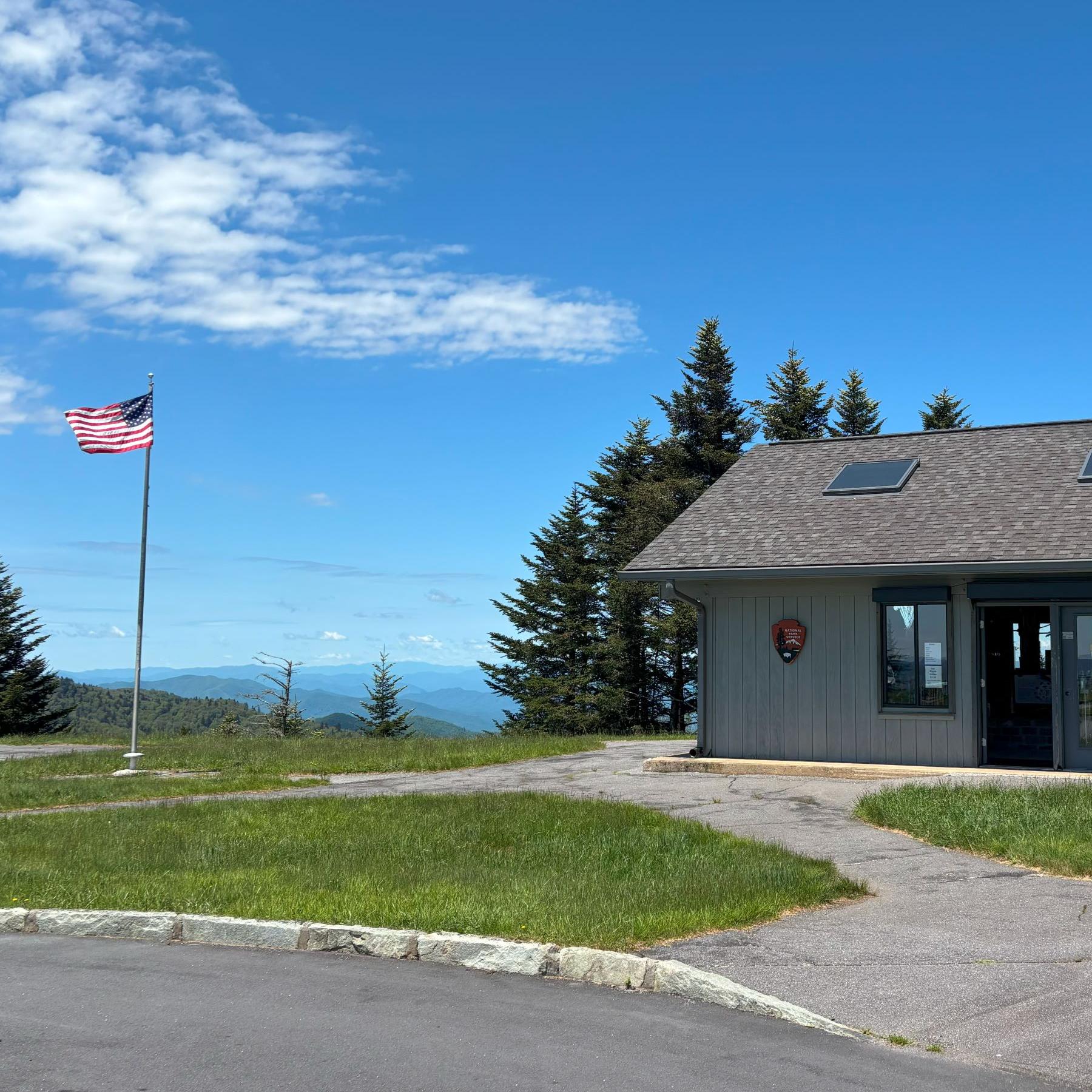 single level gray building on right side with a flagpole with American flag fluttering on left.