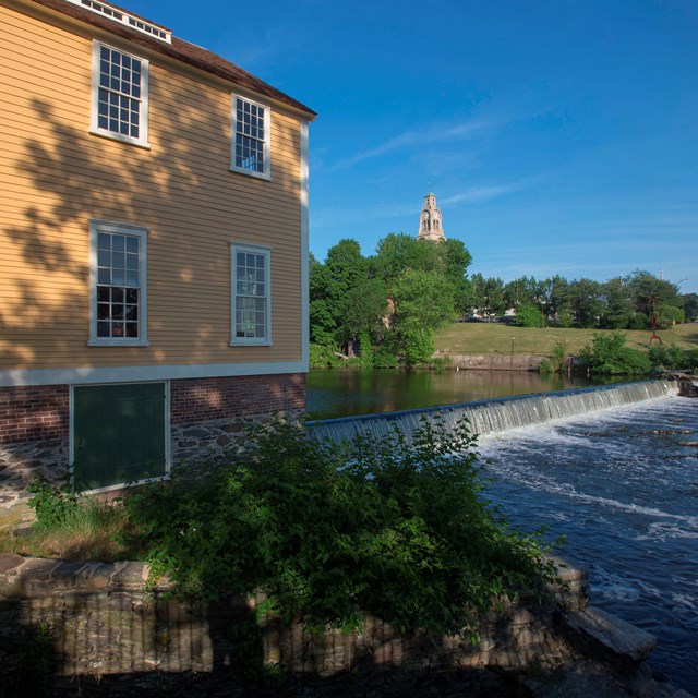 Slater Mill Dam across the Blackstone River causing waterfall and yellow wooden building on left