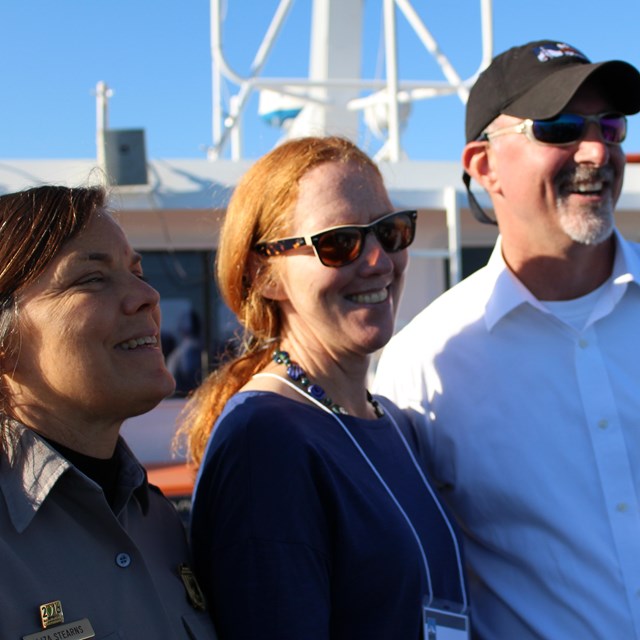 Three staff stand on a boat in the sun.