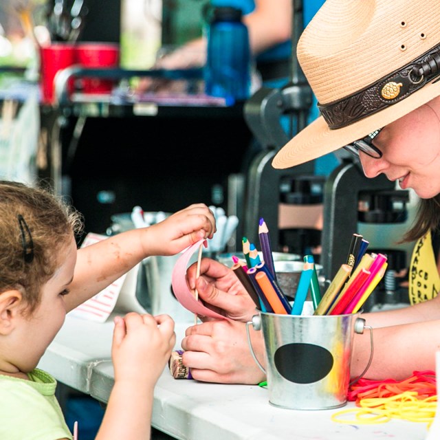 A female park ranger interacts with a young girl at a trivia wheel