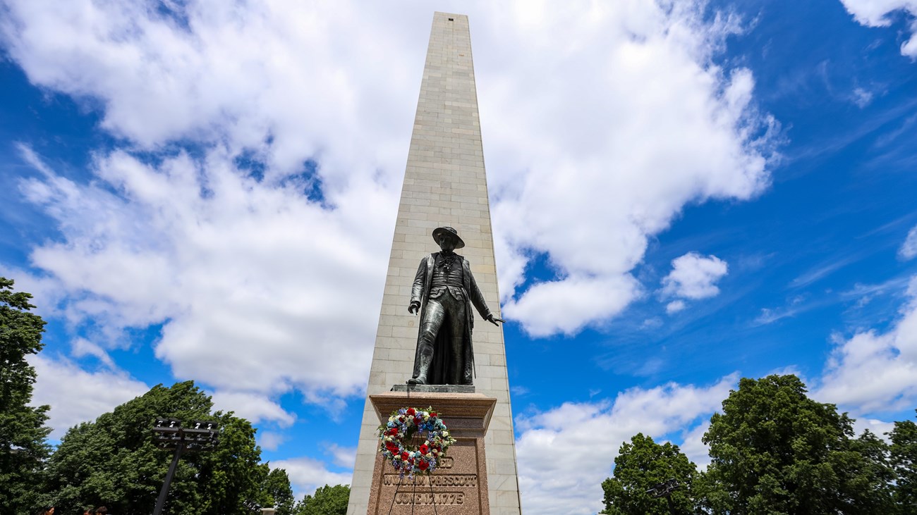 Bunker Hill Monument with the Prescott Statue before it. On a stand in front is a wreath.