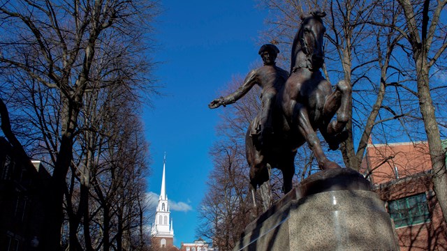 Statue of a man on horseback waving his arm. In the background is a white steeple.