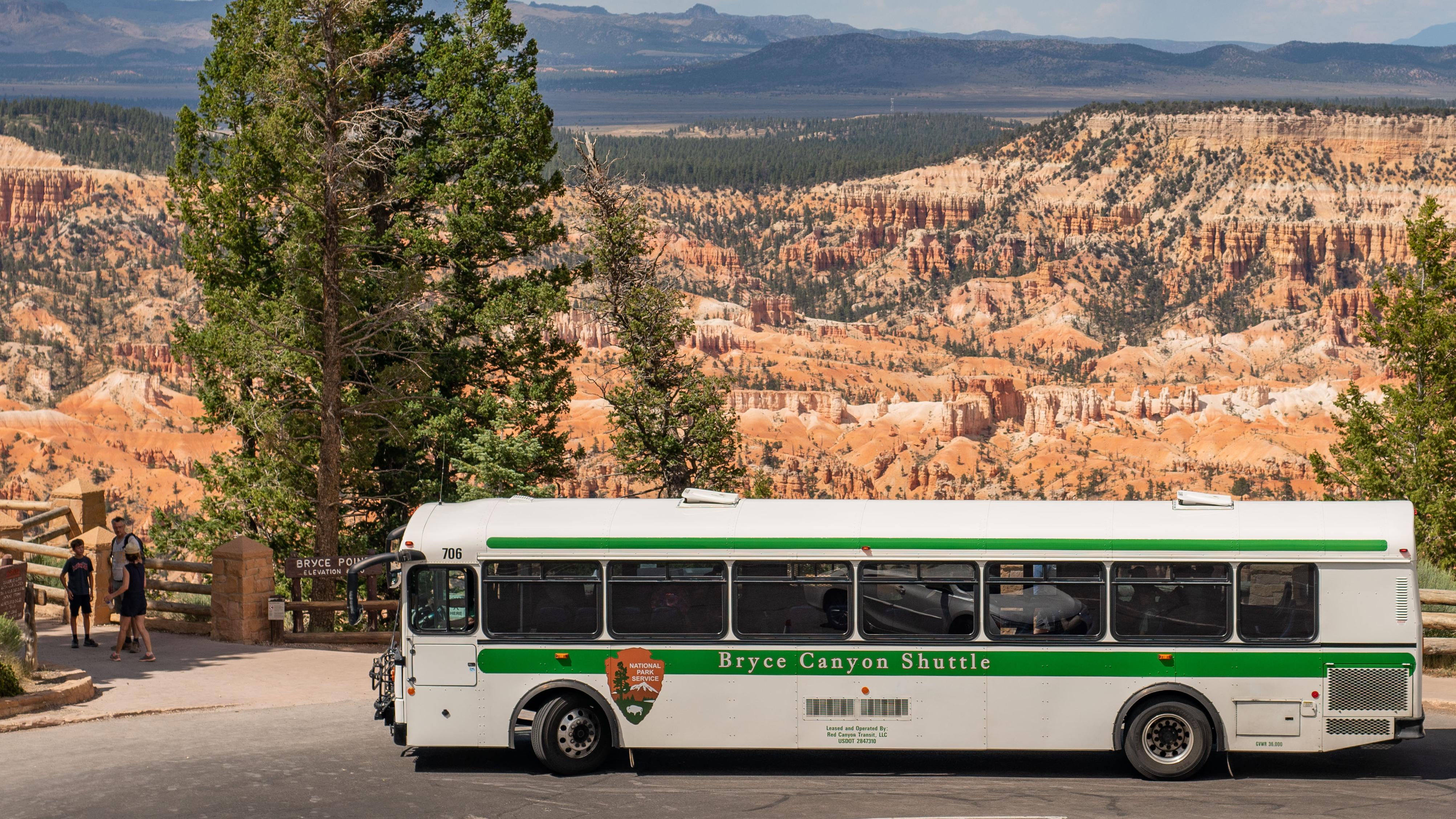 A large bus in a parking lot against a background of red rocks
