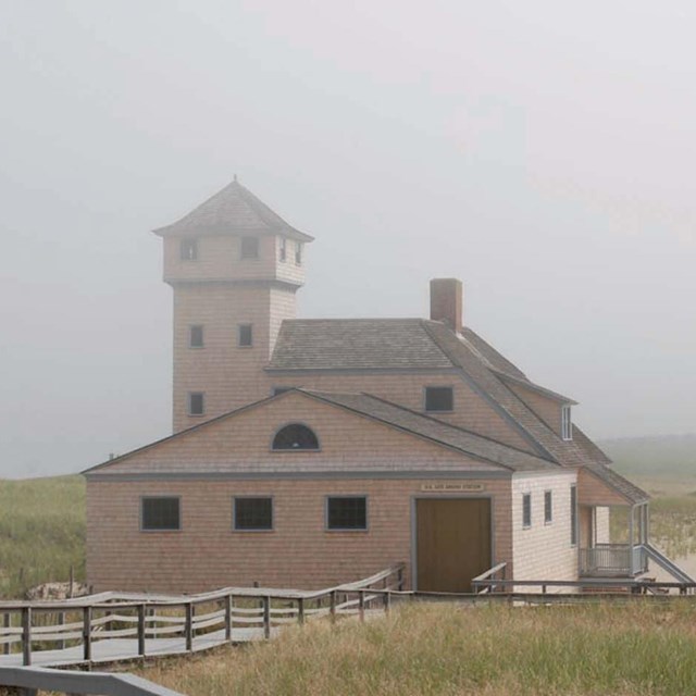An older building on a dune surrounded by mist.