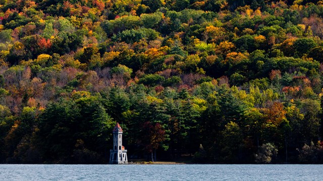 A castle tower on the edge of a lake with fall foliage. 