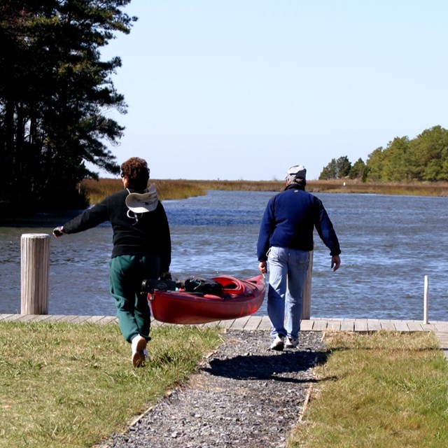 Two people carry a kayak towards a boat launch. 