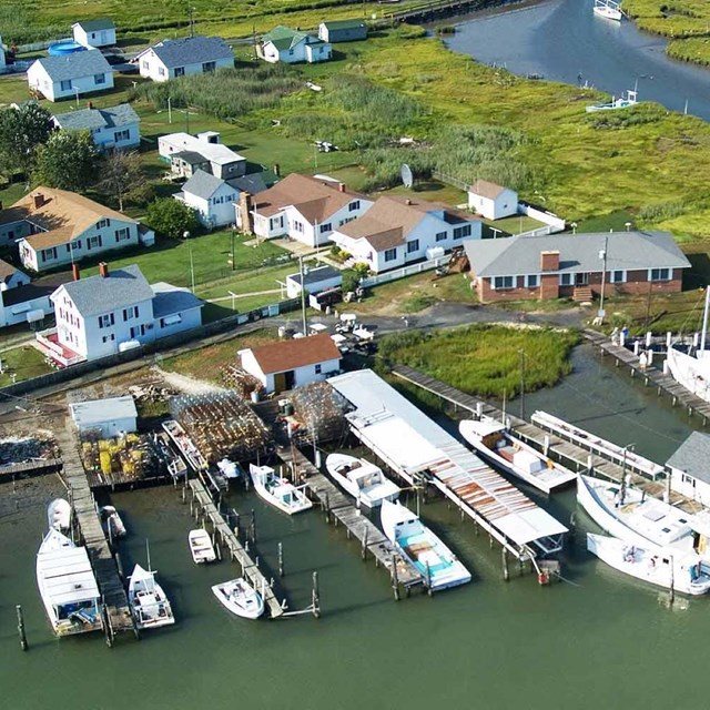 Aerial view of a marshy island with houses and small boats alongside. 