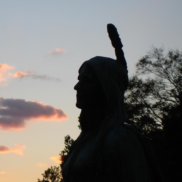 A statue of Pocahontas against a sky in sunset. 