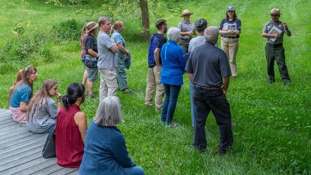 Ranger showing an image to crowd of visitors in green cemetery field.