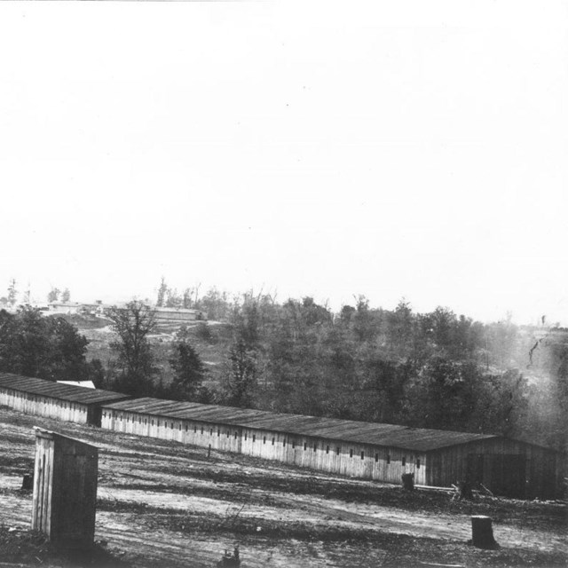Long wooden building in field with trees in the background during the Civil War.