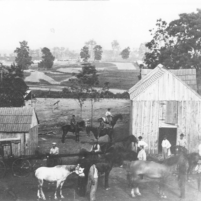 Men, horses, and a few buildings in the foreground with an earthen fort in the background,