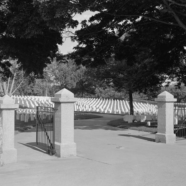 Stone gate of cemetery with white headstones in the background.