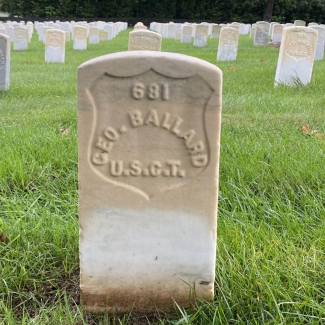 Headstone inscribed with the name George Ballard U.S.C.T. Rows of headstones in the background.