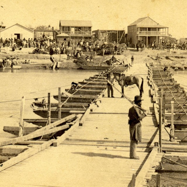 An African American soldier stands guard on a pontoon bridge that spans a Texas river in 1866.