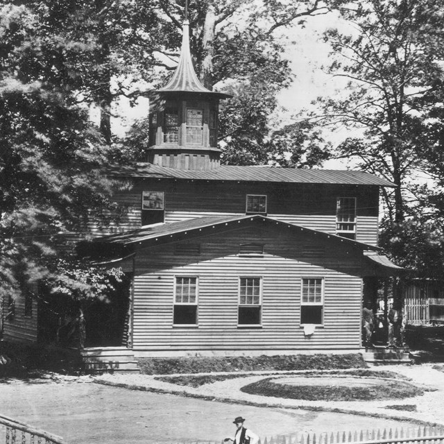 Two-story wooden building with a fence in front and surrounded by trees during the Civil War.