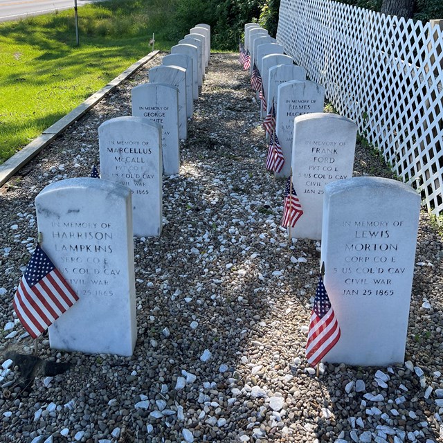Two rows of white gravestones with small American flags next to each one.