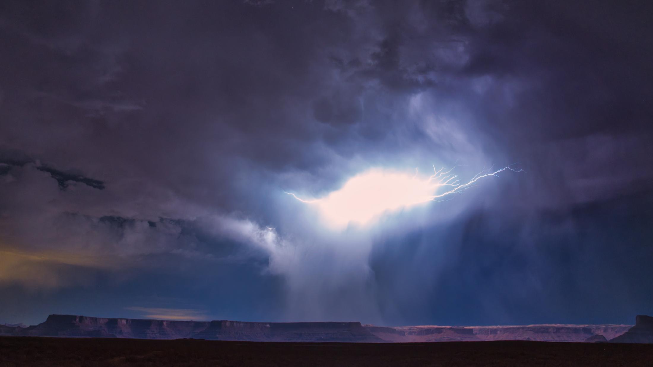 Dark clouds and lightning above a desert landscape with mesas