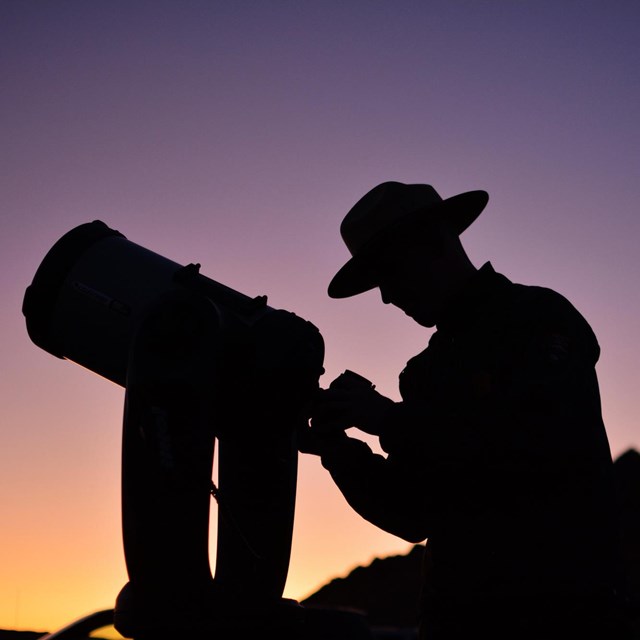 A ranger looks through a telescope at dusk