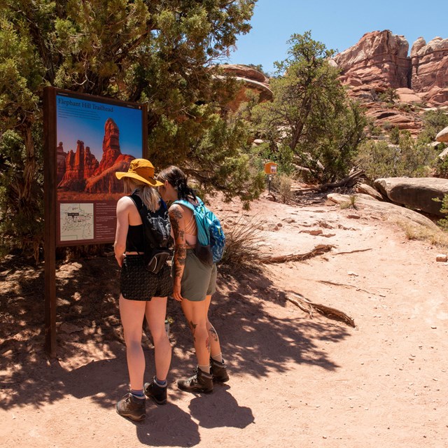 Two hikers read a trailhead sign before beginning their hike