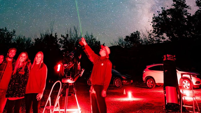 A Park Ranger stands by a telescope and points out celestial objects with a laser pointer to a crowd