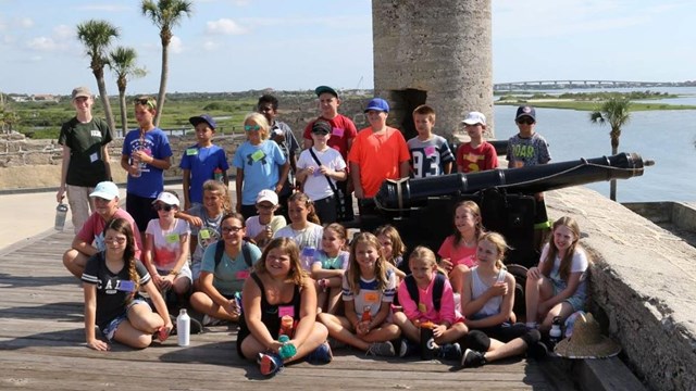 Field trip of students on gun deck near cannon and bell tower. 