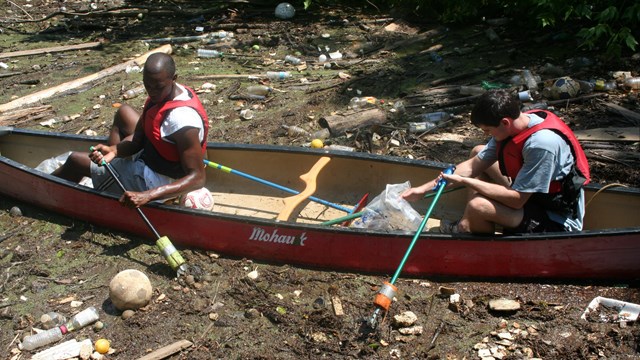 Two Volunteers sitting in a canoe picking trash out of the river.