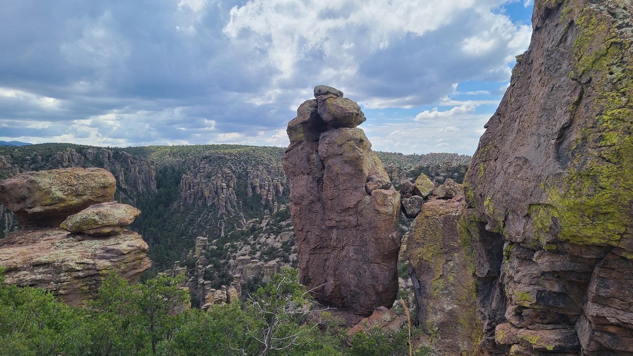 several large, jagged upright rocks stand in front of valley of pinnacle rocks with trees and sky