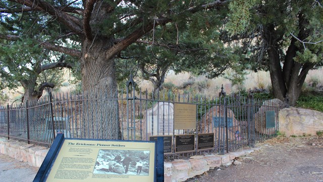 sign about settlers in front of black fence and grave stones under tree