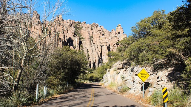 large rocks tower over roadway with falling rocks sign and trees