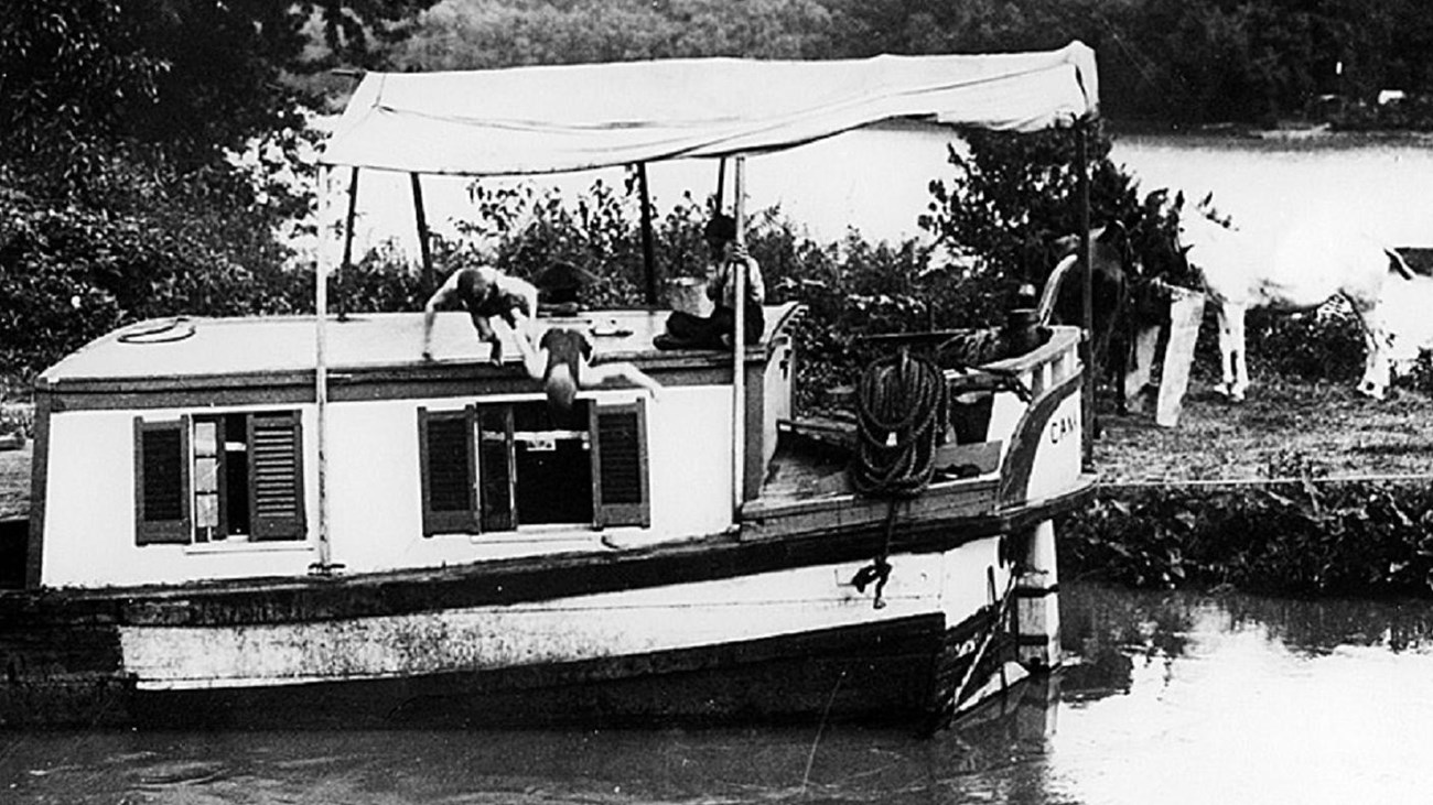 Two boys diving off a canal boat while it was tied up for the mules to feed on the tow path from the