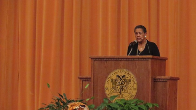 A woman speaks behind a podium with a stuffed tiger laying in front.